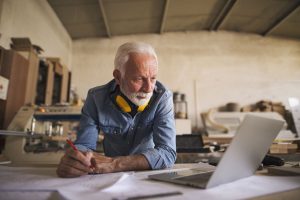 Close up of a senior architect looking at the laptop and making changes on the blueprint
